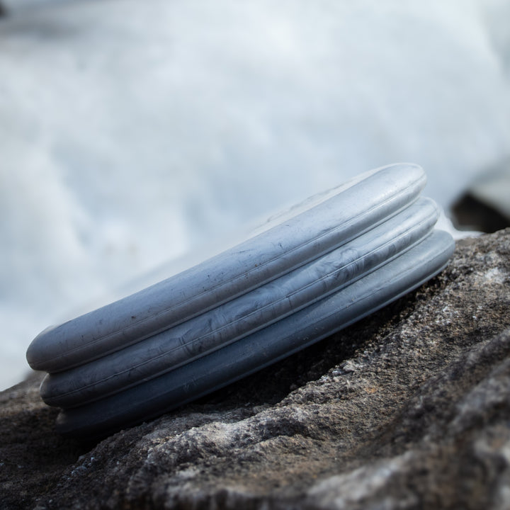 The Wizard - Lunar, a silver disc-shaped putt & approach disc with ridged edges resembling the original Wizard, rests on a rough gray rock surface outdoors.