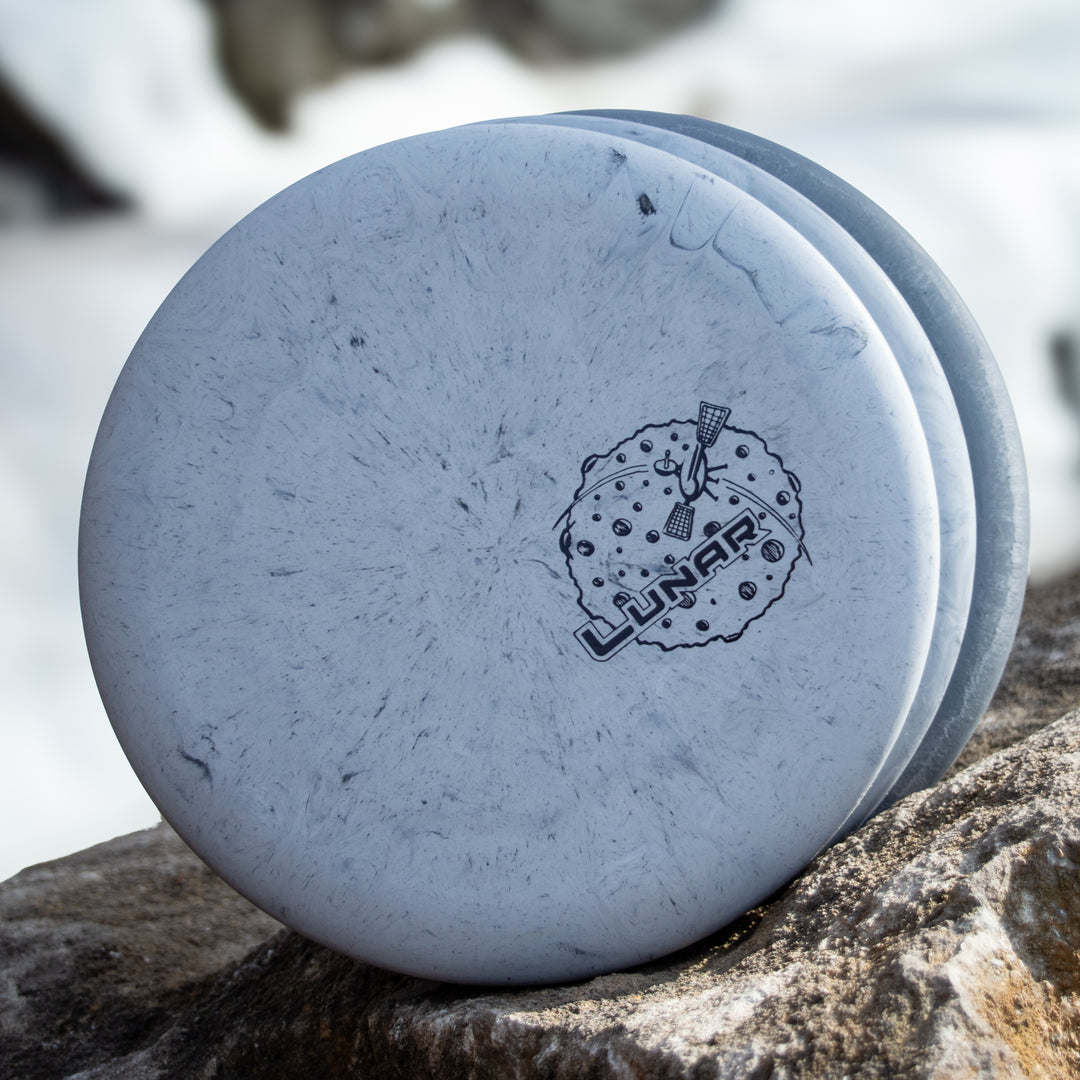 Three white Wizard - Lunar putt & approach discs in SSS plastic, each with a lunar logo and moon graphic, stacked on a rock outdoors.