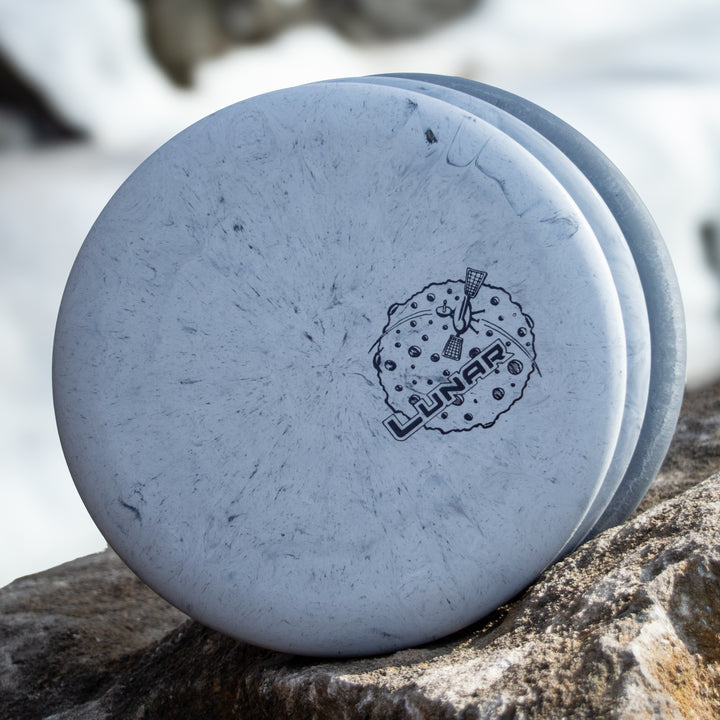 Three white Wizard - Lunar putt & approach discs in SSS plastic, each with a lunar logo and moon graphic, stacked on a rock outdoors.