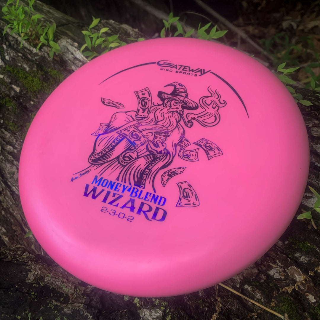 A pink Gateway "Wizard - Money" putter, known for accuracy and stability, sits on a mossy log featuring artwork of a wizard and flying money.