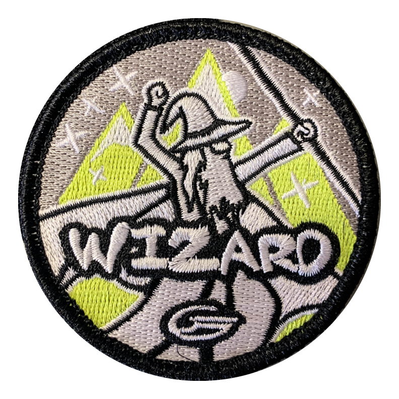 The Wizard Velcro Patch is a 3" circular patch with a bearded wizard raising his arms before mountain and star scenery, "WIZARD" embroidered below€”ideal for your Gateway Tour bag.