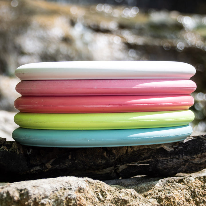 A stack of five Wizard - Multi Flex 5 pack discs in white, pink, green, and blue sits on a rock against a blurred outdoor background.