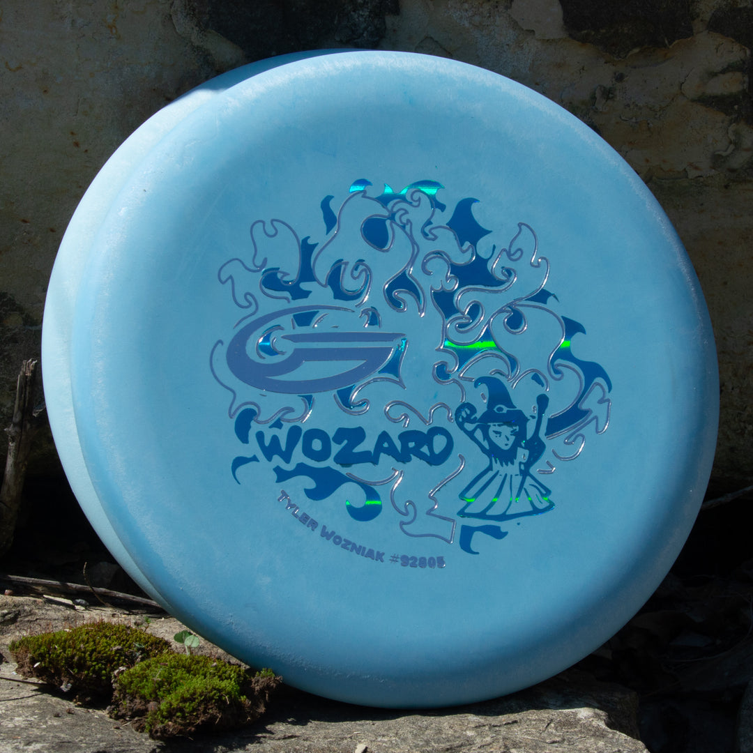 Tyler Wozniak's "Wozard" - Nylon Alloy is a blue disc golf disc featuring a wizard graphic and abstract designs, with "WOZARD" printed on it—ideal for tee shots or consistent mid-range drives.