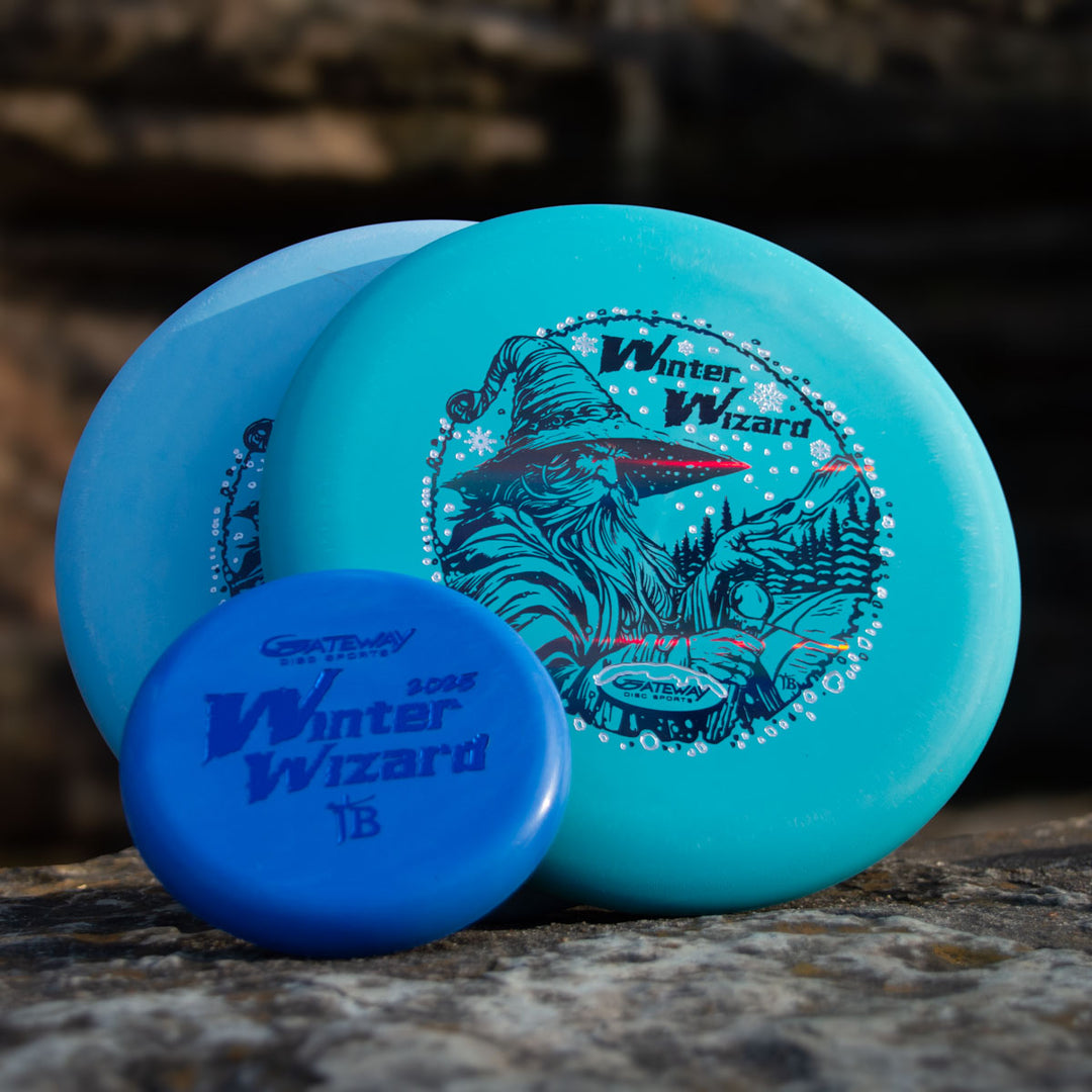 The 2-Disc Players Pack - Winter Wizards 2025, featuring blue Wizard discs with custom wizard graphics, is displayed outdoors on a rock. Two large discs and one smaller disc are shown in front.