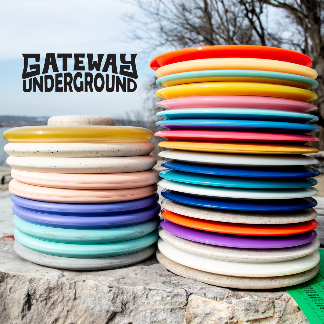 Two tall stacks of Gateway Factory 2nd Mystery 30-Pack discs, featuring drivers and putters, are arranged outdoors on a stone surface with "Gateway Underground" text in the background.