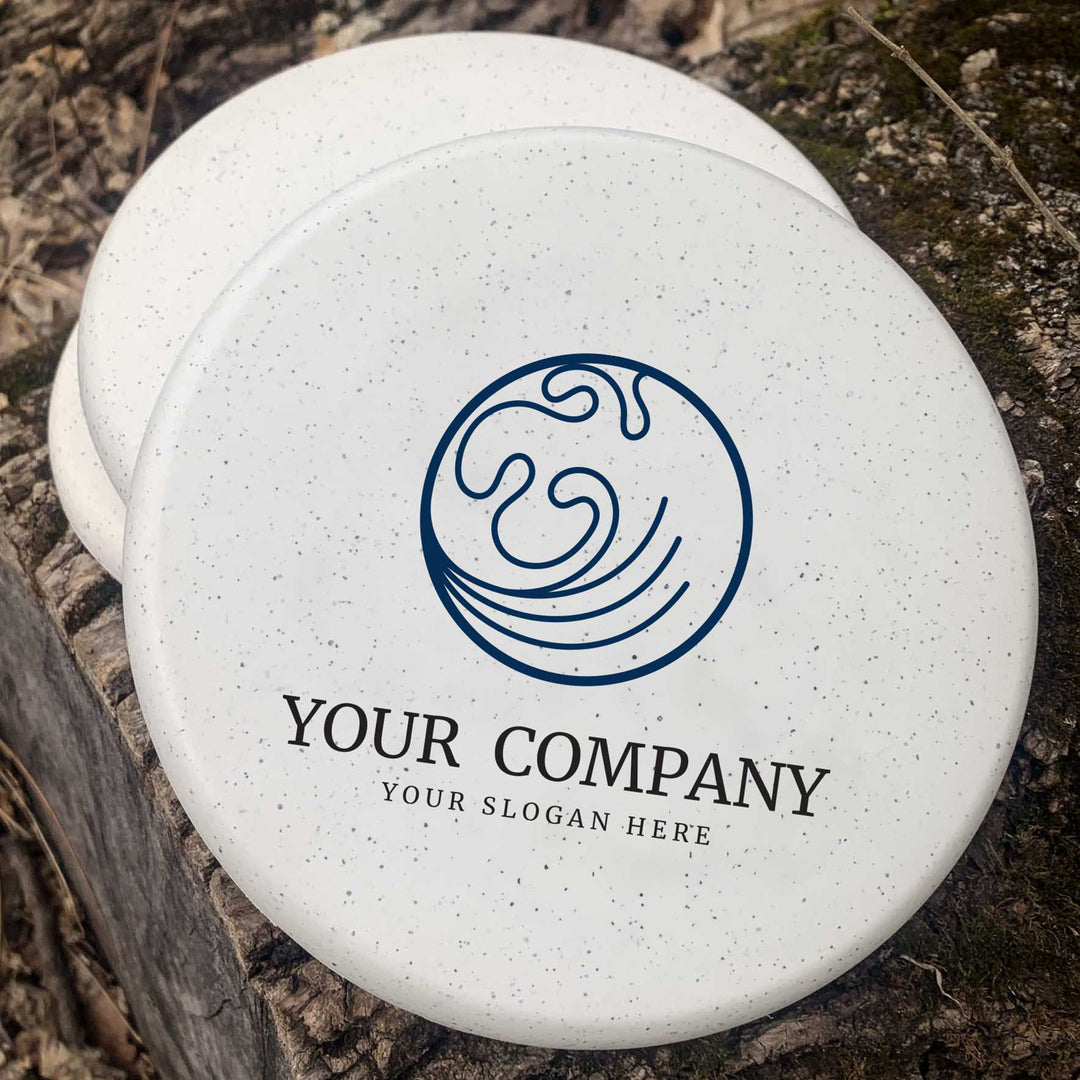 Two white Custom Diamond Lil Wizard discs, stamped with a blue abstract globe and "YOUR COMPANY YOUR SLOGAN HERE," sit on a tree stump outdoors€”ideal as unique corporate gifts or wedding favors.