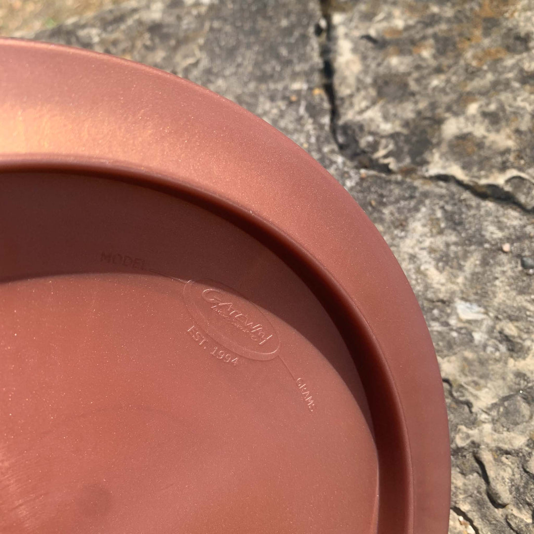 A close-up of a brown plastic Apex - Diamond disc golf disc on stone pavement, featuring the "Gateway" logo and embossed manufacturing details on the underside—designed for stable flight.