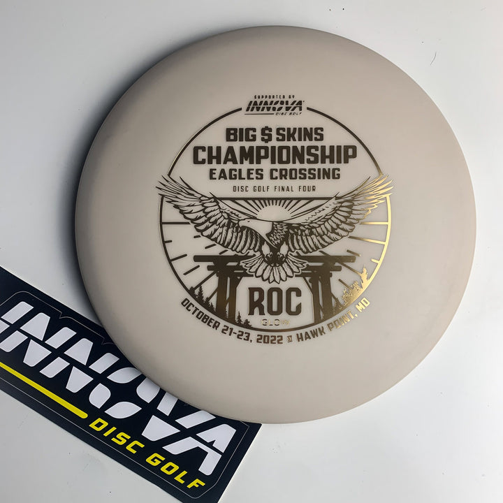 A white EC Innova Roc DX Glow disc with "Big $ Skins Championship Eagles Crossing" and an eagle graphic, plus an INNOVA logo sticker.