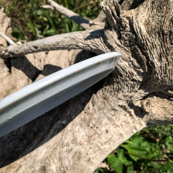 A Blaze - Hyper Diamond (HD) Hemp white overstable driver sits on a weathered tree trunk outdoors, green grass behind it—ideal for reliable drives and great control, even in strong headwinds.