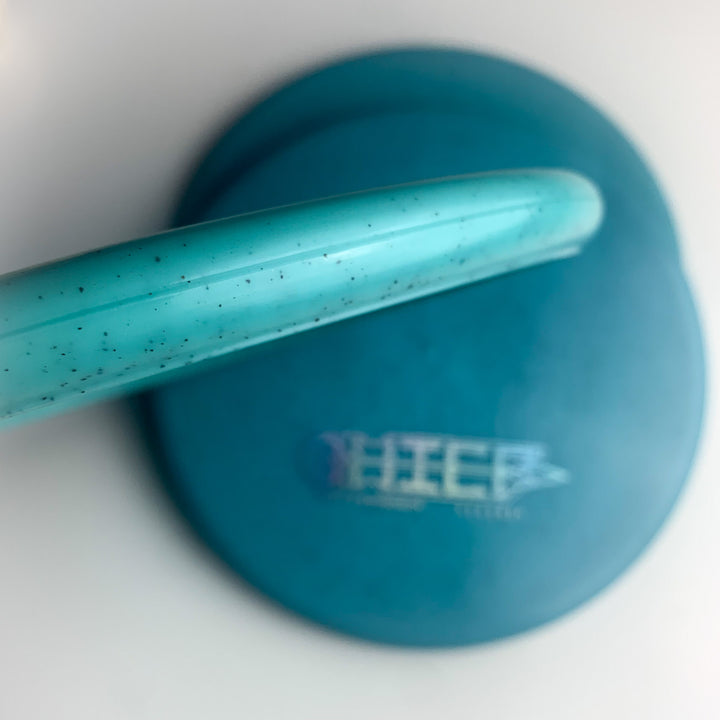 A close-up of a teal circular case with a matching low profile lid placed diagonally on top, displaying the words "Chief - Diamond Hemp" in blurred white text.