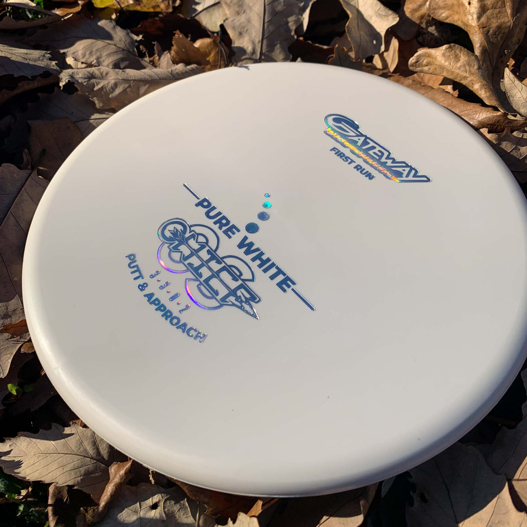 A Chief OS - Pure White disc golf putter, made from Pure White Premium Suregrip Plastic and marked "PURE WHITE" and "PUTT & APPROACH," rests on brown fallen leaves.