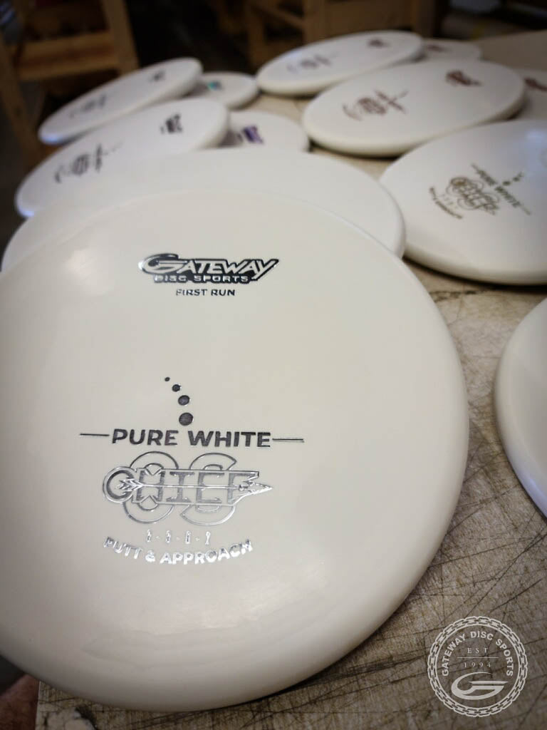 Multiple white Chief OS - Pure White discs by Gateway Disc Sports, made from Pure White Premium Suregrip Plastic, are stacked on a table with "Chief OS" and —Putt & Approach—� branding visible, emphasizing this overstable model.