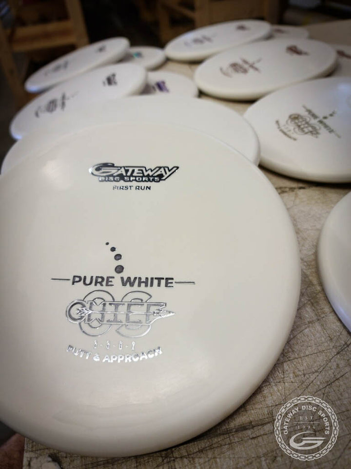 Multiple white Chief OS - Pure White discs by Gateway Disc Sports, made from Pure White Premium Suregrip Plastic, are stacked on a table with "Chief OS" and —Putt & Approach—� branding visible, emphasizing this overstable model.