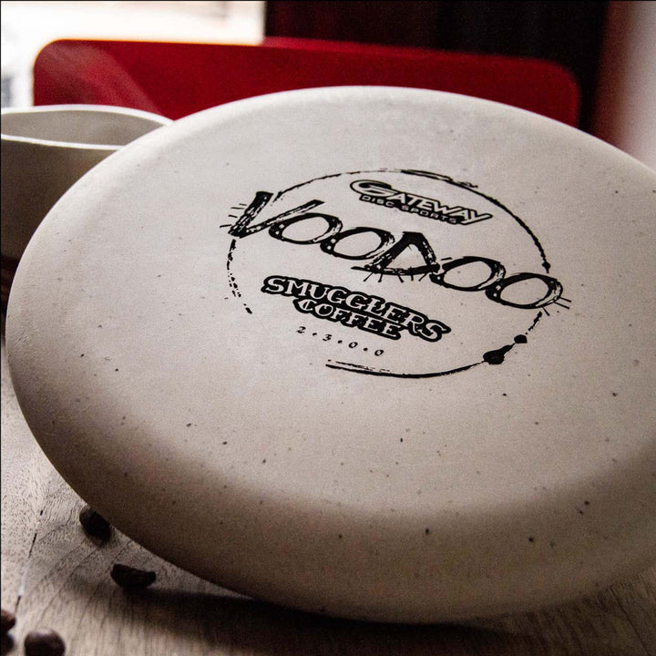 A close-up of a white lay-up disc golf disc, the "Voodoo - Smugglers Coffee Special Blend," featuring black text for the branding and celebrating Smugglers Coffee's signature espresso blend.