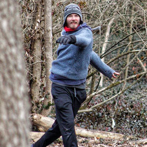 Wearing a knit hat, gloves, and sweater, a person throws a disc in the woods during a Disc Golf Lesson.