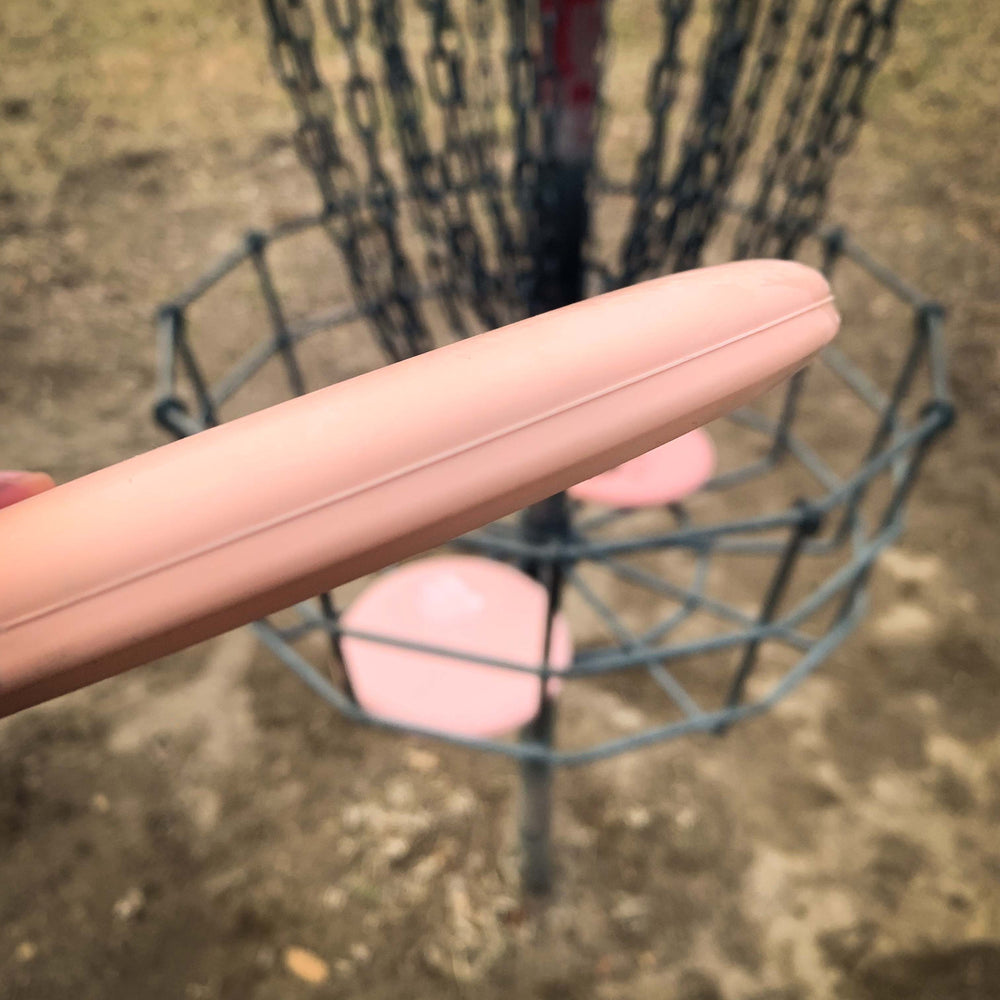 A close-up view shows a hand holding a Magic - Eraser beginner-friendly putter disc golf disc near a basket with chains and several discs inside.