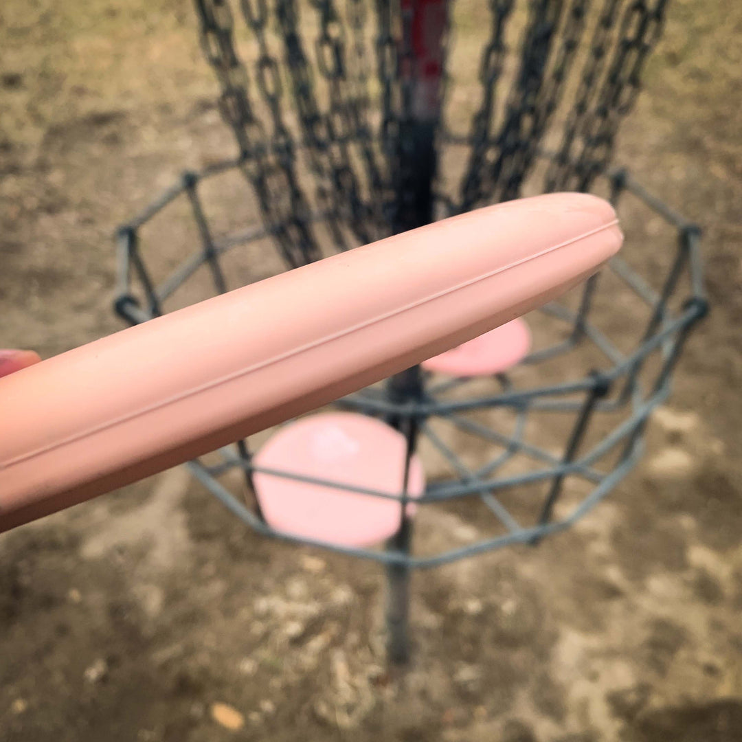 A close-up view shows a hand holding a Magic - Eraser beginner-friendly putter disc golf disc near a basket with chains and several discs inside.