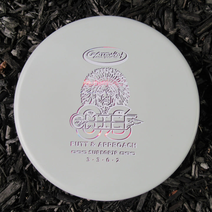 A white Gateway Chief OS - Suregrip disc golf putter with a hedgehog design and "Chief" plus "Putt & Approach" printed on it, resting on dark mulch—perfect for hyzer lines and dependable approaches.