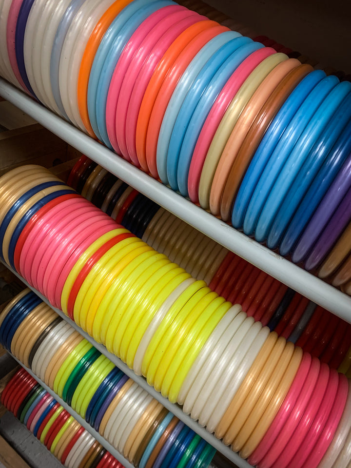 Rows of colorful Chief OS - Diamond plastic discs are stacked vertically on metal shelves, showcasing a range of bright and pastel colors—perfect for forehand drives or reliable overstable hyzer throws.