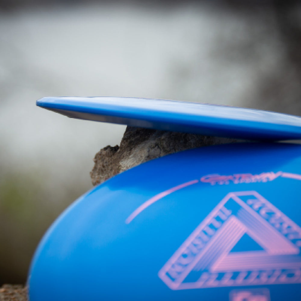 Close-up of two Illusion - Cobalt disc golf discs stacked at an angle outdoors, one resting on the edge of the other—ideal for easy distance throws.