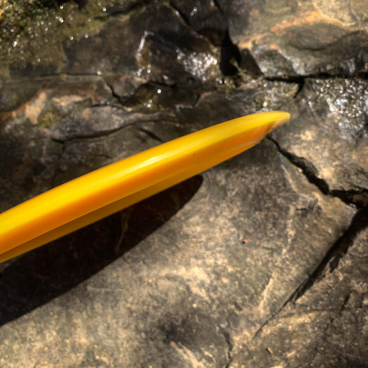 A close-up of the yellow tip of the Journey - Hyper Diamond (HD) long-range distance driver resting on sunlit, textured rocks.