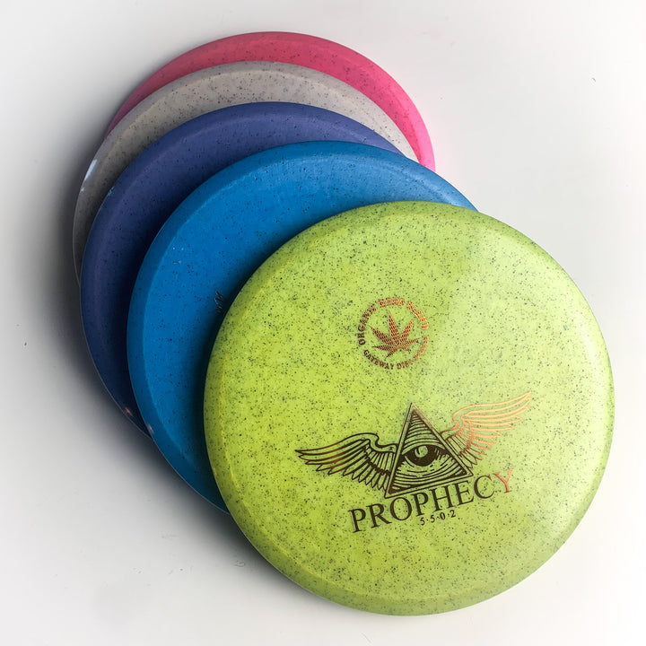 Five stacked "Prophecy - Diamond Hemp" disc golf discs in green, blue, purple, gray, and pink; the top disc shows an all-seeing eye graphic. Made from premium Diamond Hemp blend for consistent flight as an overstable mid-range.