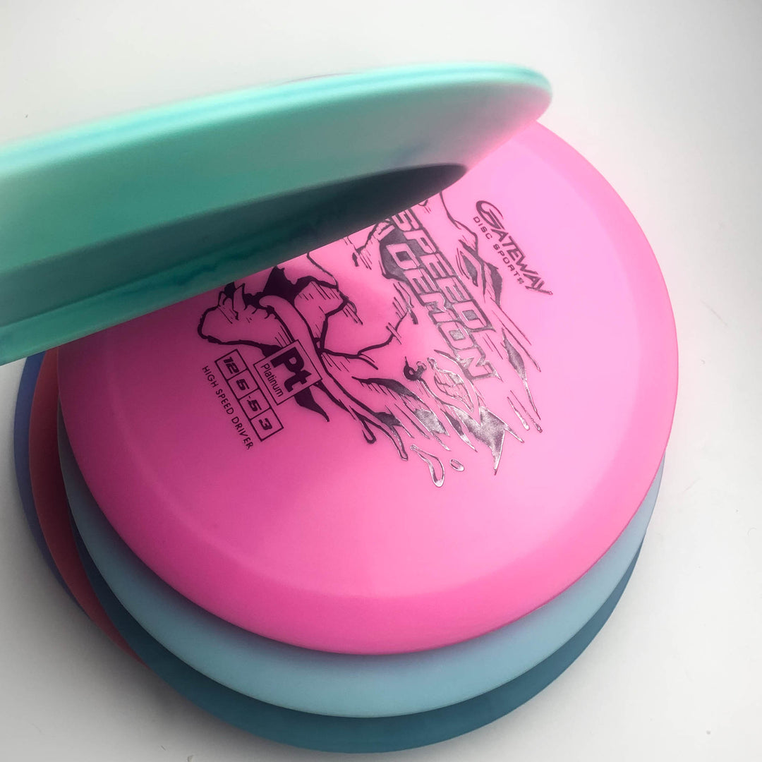 A stack of four disc golf discs in pink, teal, light blue, and blue, with the top disc showing —Speed Demon - Platinum—� branding—ideal for power forehands or backhand flex shots with your go-to overstable driver.