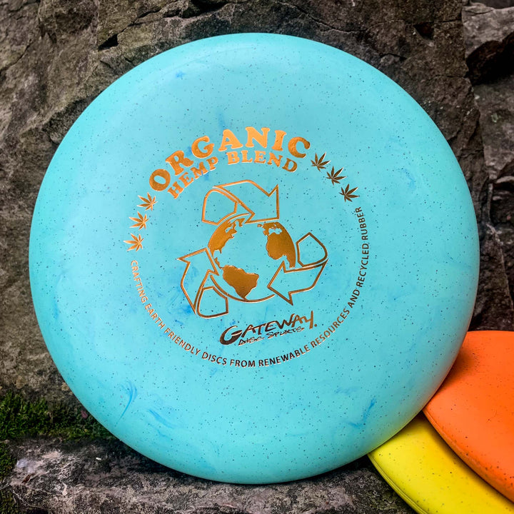 A Gateway Warlock - Organic Hemp (H-SS) putter disc with eco-themed graphics rests on a rock, next to orange and yellow discs, offering an earth-friendly choice to improve your approach game.