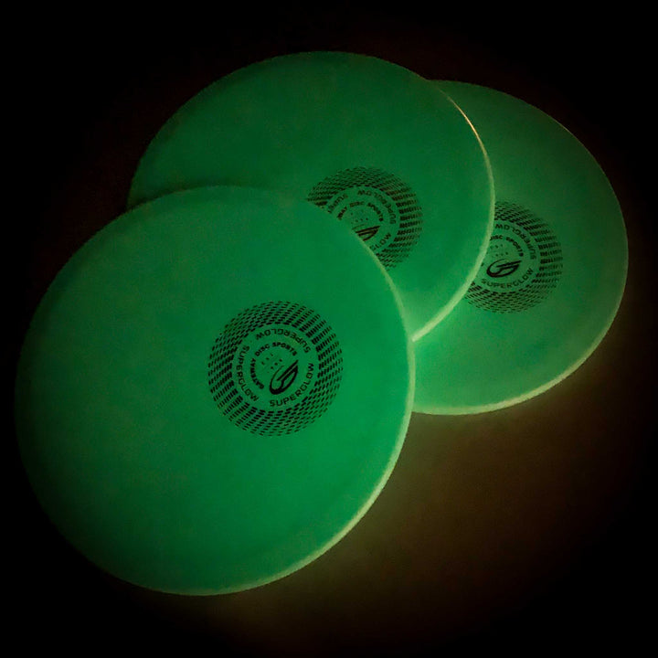 Three Warrior - SureGrip™ Superglow mid-range discs, green and glow-in-the-dark with circular logos, are overlapped against a dark background.
