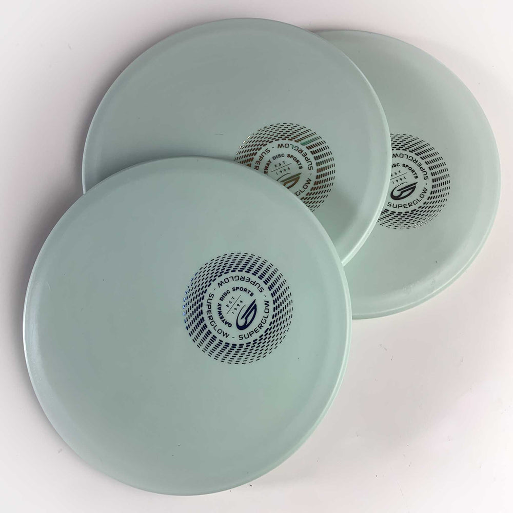 Three Warrior - SureGrip™ Superglow discs in light blue—perfect for hyzer approaches—showcase black and gold circular logos, overlapping on a white background.