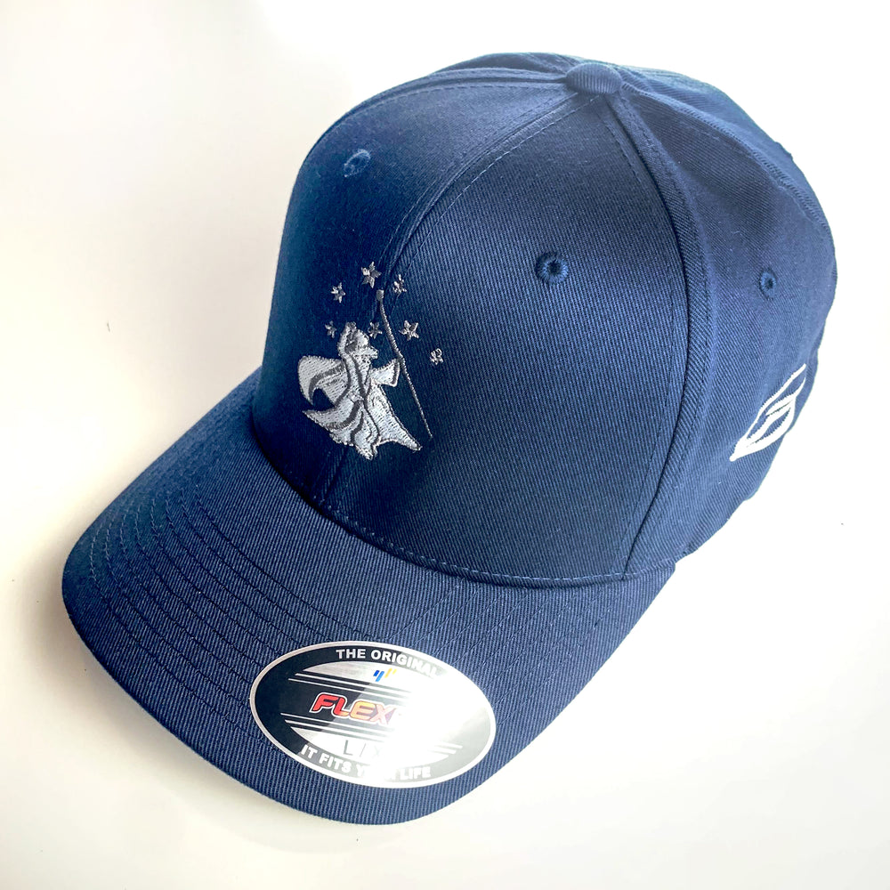 The Wizard Flexfit Fitted Hat in navy blue features an embroidered bird and stars logo on the front, a white Mini-Wizard logo on the side, and a Wizard bar stamp detail, shown displayed on a white surface.