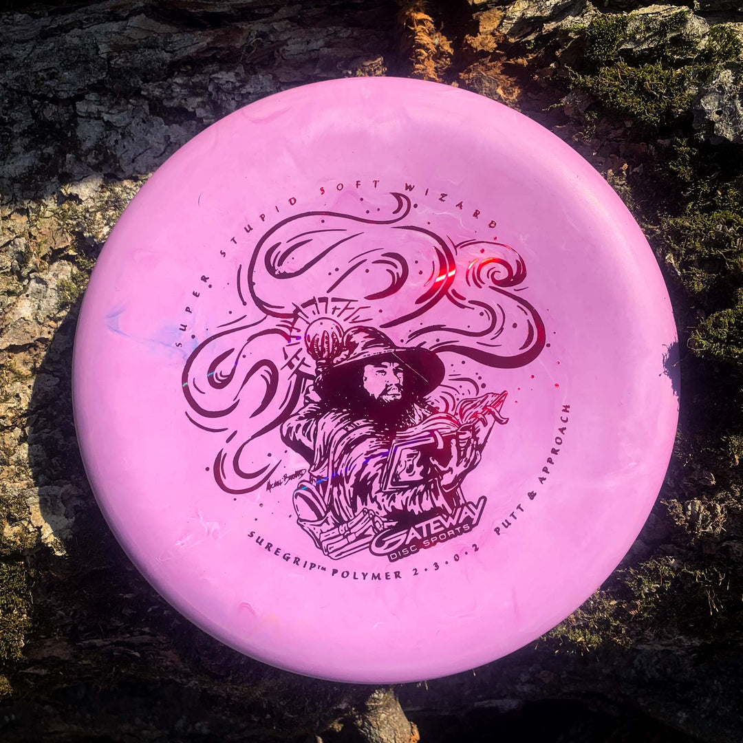 The Wizard - SSS is a pink, stable putter with an illustrated wizard holding a staff on a textured tree bark background—ideal for accurate throws and dependable performance in windy conditions.