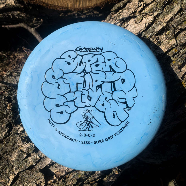 A blue Wizard - SSSS, an overstable disc golf putter, rests on rough tree bark in sunlight.