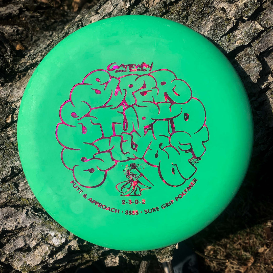 A green Wizard - SSSS putter with beaded putt and approach design rests on rough tree bark, featuring stylized red lettering and detailed specs on its surface.