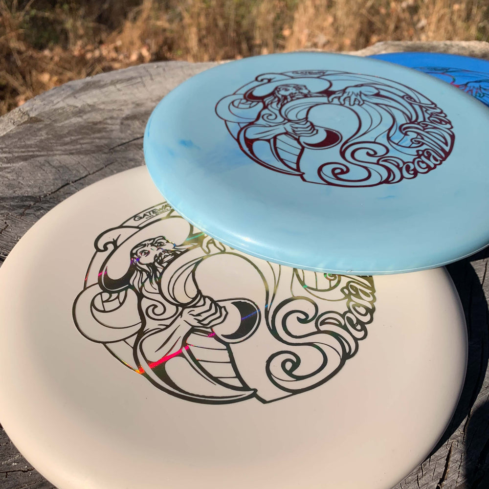 Two Wizard - Special Blend putters with intricate designs sit on a tree stump outdoors, framed by dry grass. These stable workhorse putters offer reliability and style, making them ideal for players who value consistency in their game.