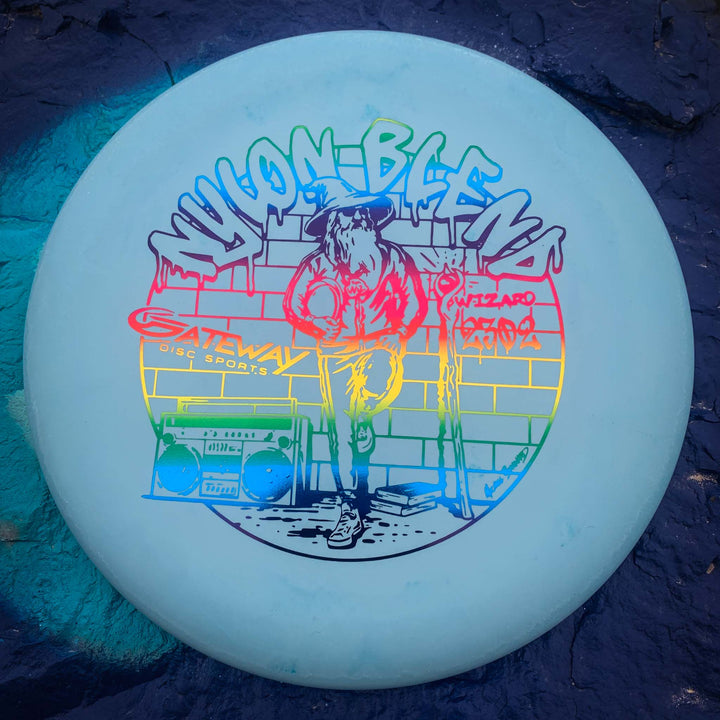 The Wizard - Suregrip Nylon is a stable, light blue disc golf putter featuring a rainbow graphic of a person in a hoodie, brick wall, boombox, and "Nylon Blend" and "Gateway Disc Sports" text—ideal for reliable mid-range drives.
