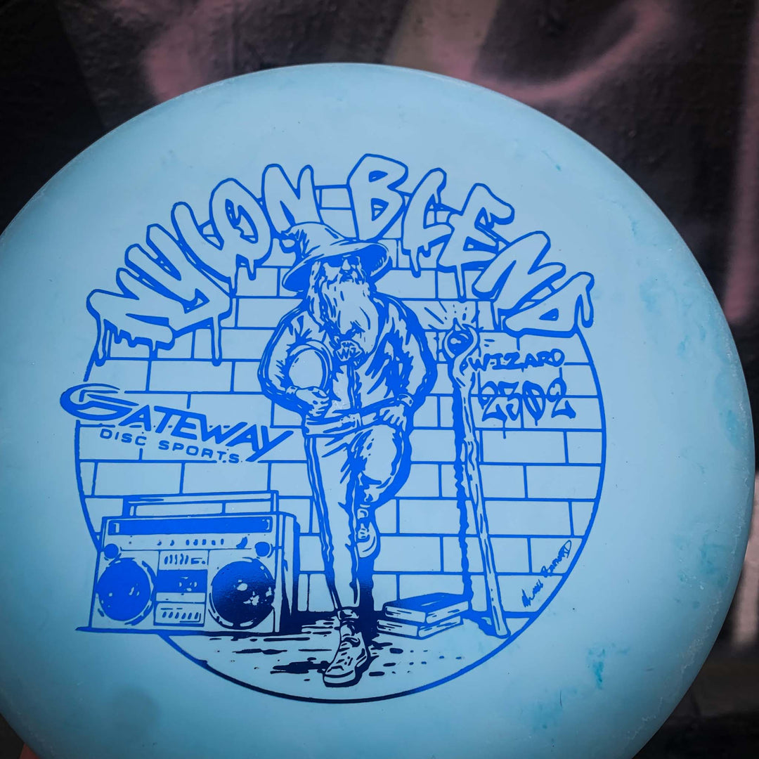 Light blue Wizard - Suregrip Nylon disc golf disc featuring a Wizard with a disc and staff by a brick wall and boombox. Text: "NYLON BLEND," "Gateway Disc Sports," and "Wizard." Great for stable putts and reliable mid-range drives.