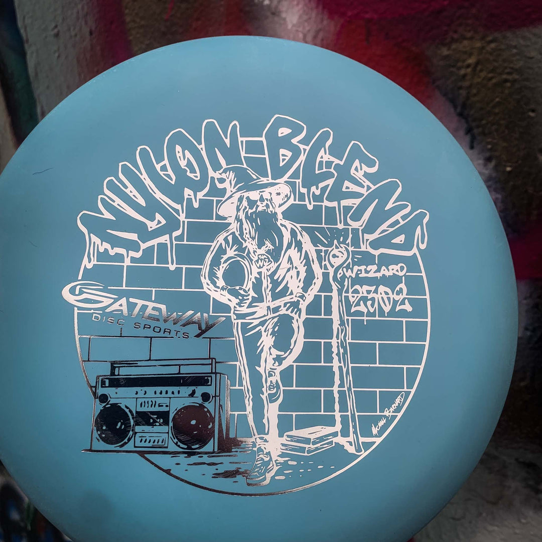 The Wizard - Suregrip Nylon is a blue disc golf disc from Gateway Disc Sports, featuring a wizard with a staff and boombox, plus graffiti "WIZARD" text. Ideal as a stable putter for confident mid-range drives.