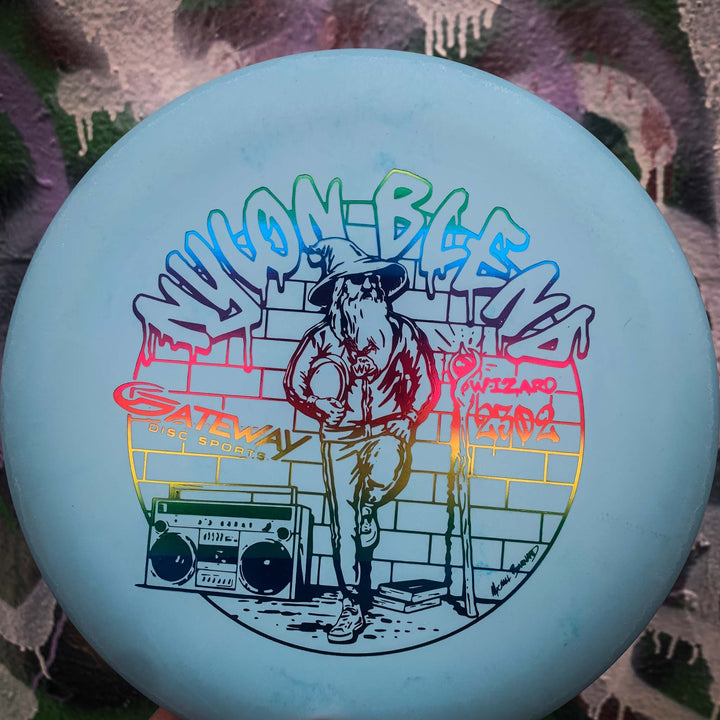The Wizard - Suregrip Nylon is a light blue disc showing the Wizard holding a disc by a boombox in front of graffiti-style "WIZARD" and "Yoonblend" text—ideal for mid-range drives or anyone needing a stable putter.