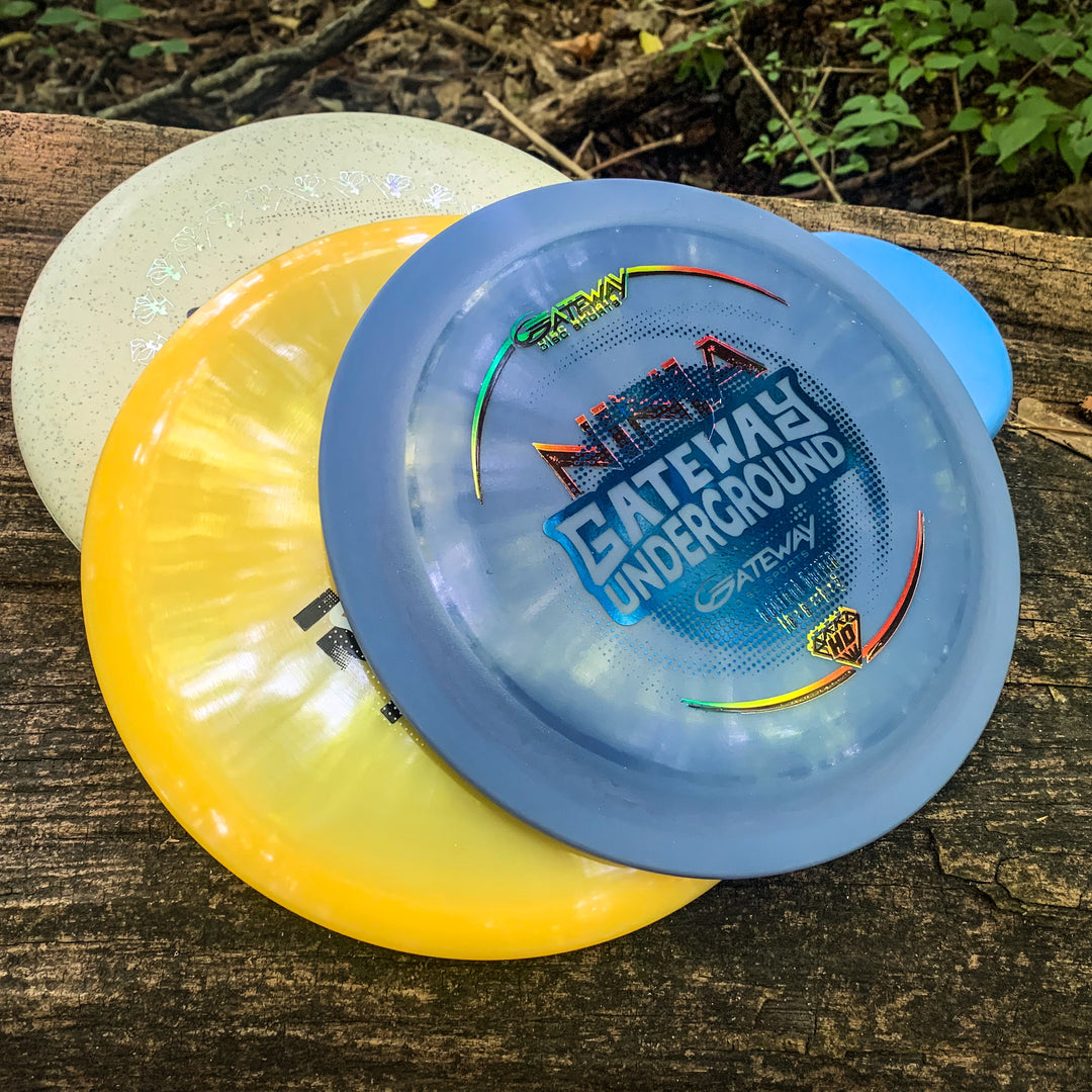 Three vibrant Factory 2nd 3-Disc Starter Pack discs, including a blue one, are stacked on a weathered wooden surface outdoors.