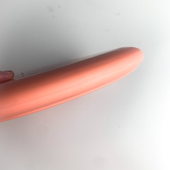 A close-up shows a person holding the edge of a round, flat, peach-colored Wizard Leaf Suregrip Putter from Gateway Disc Sports against a white background.