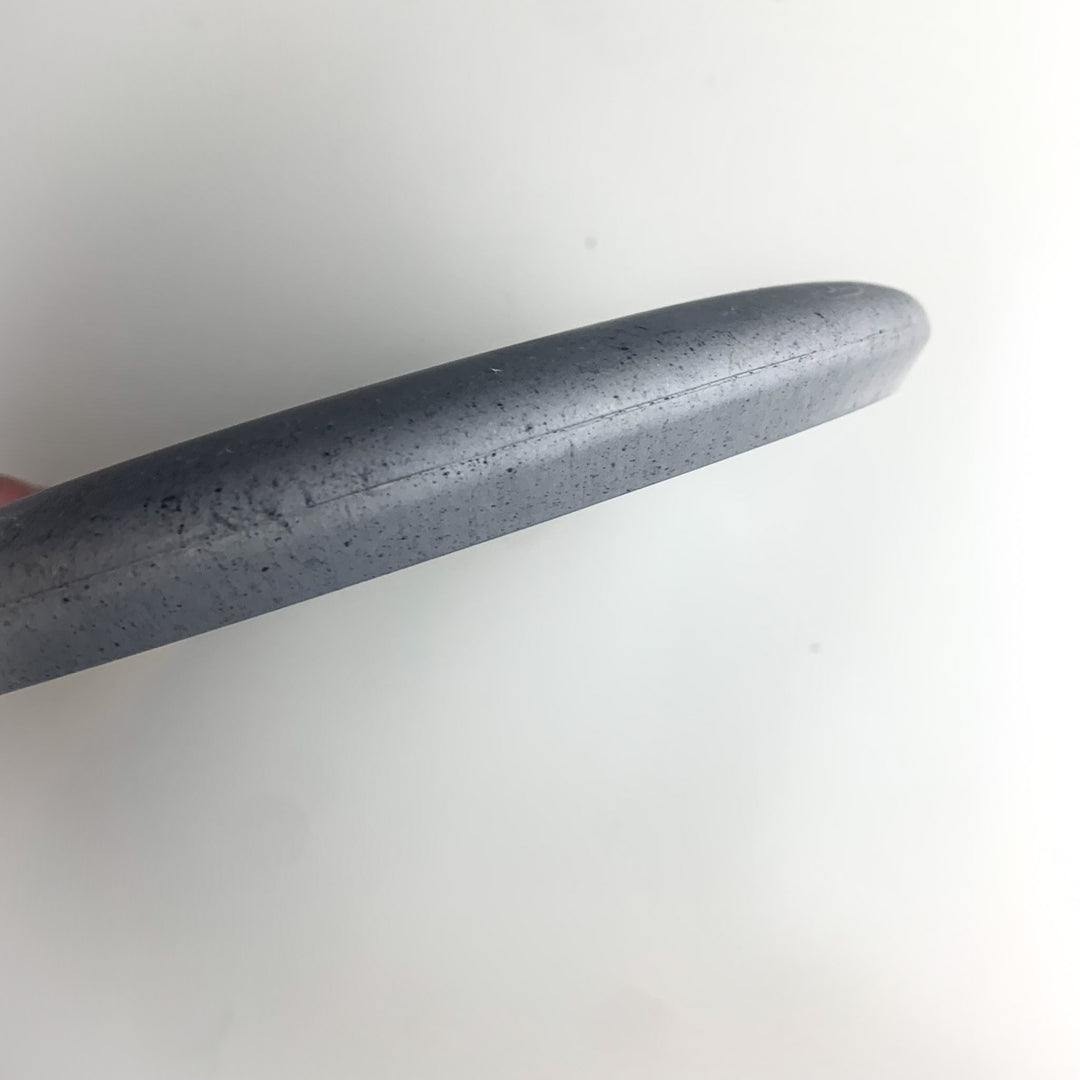 Close-up view of the edge of a gray, round Wizard Leaf Suregrip Putter with a smooth, slightly speckled surface, photographed against a plain white background.