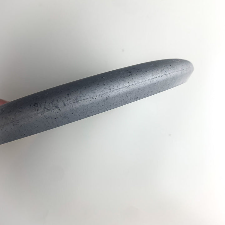 Close-up view of the edge of a gray, round Wizard Leaf Suregrip Putter with a smooth, slightly speckled surface, photographed against a plain white background.