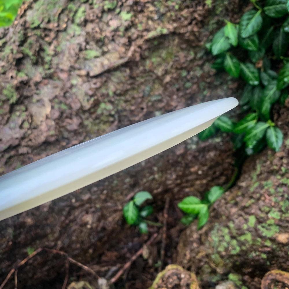 A close-up of the Blade - HD - NOT CURRENT VERSION's pointed white tip shows steady resistance against textured tree bark, with green leaves providing a natural backdrop.
