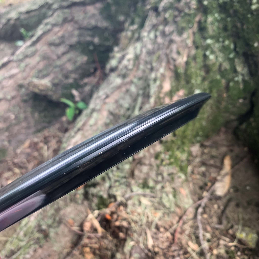 Close-up of the edge of a black Blaze - Hyper Diamond (HD) driver, held outdoors near a large tree with exposed roots—ideal for predictable drives in headwinds.