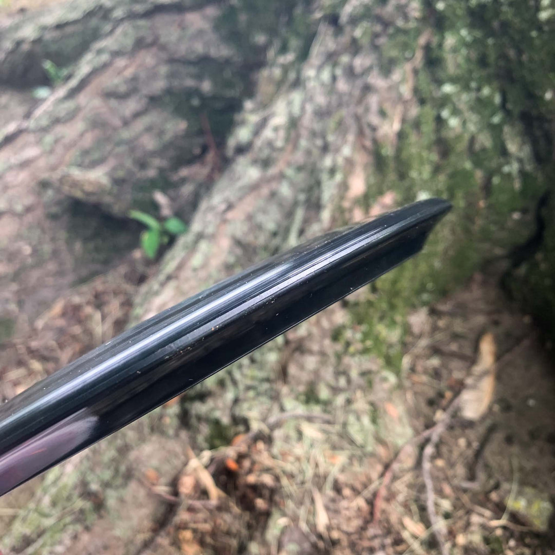 Close-up of the edge of a black Blaze - Hyper Diamond (HD) driver, held outdoors near a large tree with exposed roots—ideal for predictable drives in headwinds.