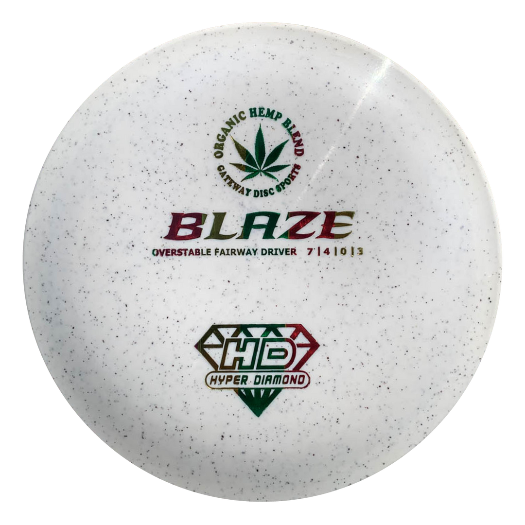 The Blaze - Hyper Diamond (HD) Hemp is a white disc golf driver with a brown and green "Organic Hemp Blend" logo, "BLAZE" text, flight numbers 7|4|1G|3—an overstable driver ideal for headwinds and consistent drives.