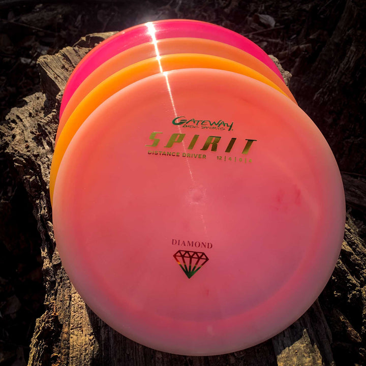 Four pink Spirit - Diamond high speed distance driver discs are stacked on a tree stump, sunlight highlighting their glossy surfaces.