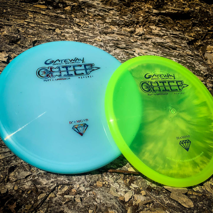 Two Chief - Diamond discs, one blue and one yellow-green, featuring a beaded rim, rest on a textured outdoor surface as sunlight casts shadows.