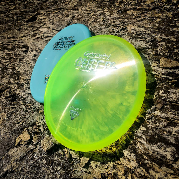 Two Chief - Diamond discs by Gateway, one blue and one translucent yellow with a beaded rim, rest on a rough-textured tree trunk outdoors in sunlight.